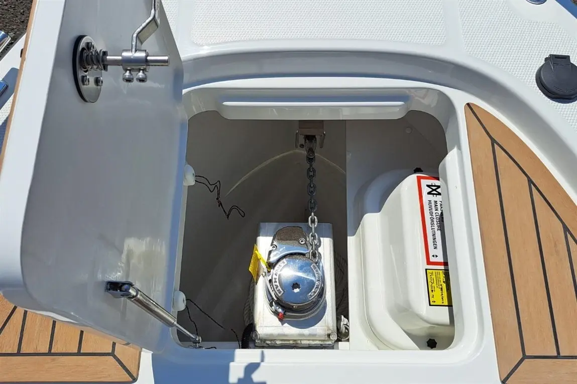 View of a boat's storage compartment featuring a winch, chain, and safety warning label. Ideal for marine enthusiasts.